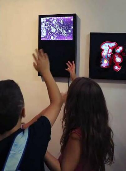 Los niños interactuando con la obra "Cielos nocturnos memorias compartidas"  Caja transiluminada con acrílico, led, arduino y sensores de movimiento. 54 x 33,3 x 7 cm. 2022 